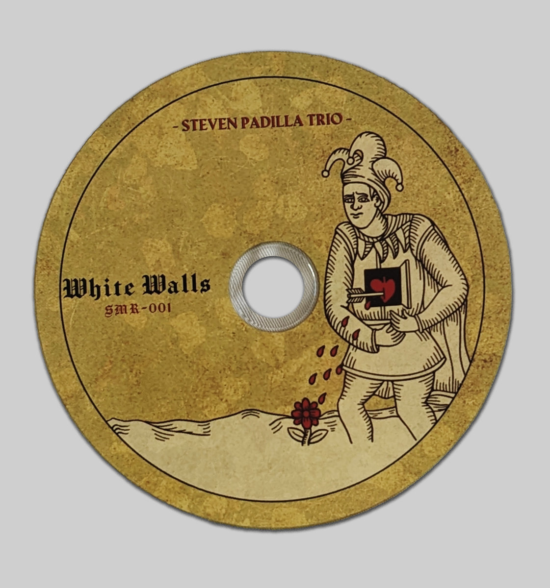 Printed compact disc, featuring a jester character in the style of tarot de merseille with an arrow through his heart over a subtle background of fallen leaves, all in a colorscheme of red and gold